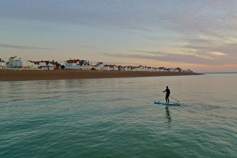 A lone paddleboarder on a calm sea with Deal beach and seafront in the background. 