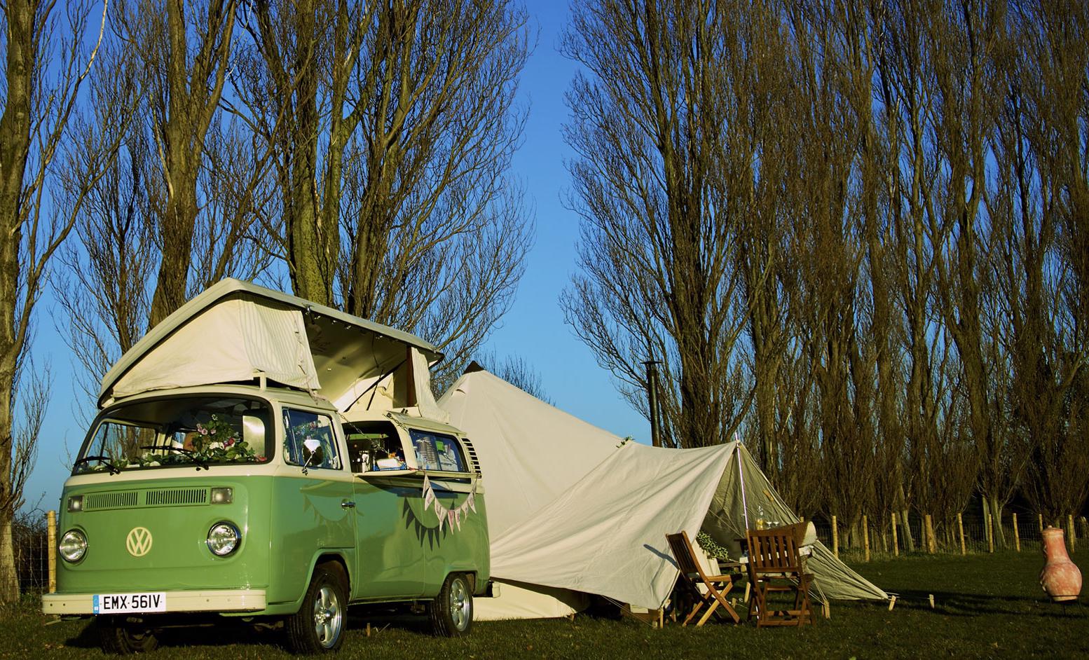 camper van pitched in field with trees