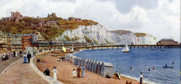 A colour illustration of Dover seafront in the 1900s with beach huts on the beach and the cliffs and castle in the background