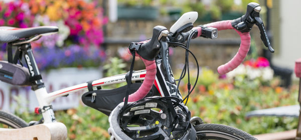 A racing bike and helmet leant against a bench with pink, orange and purple flowers in the background.